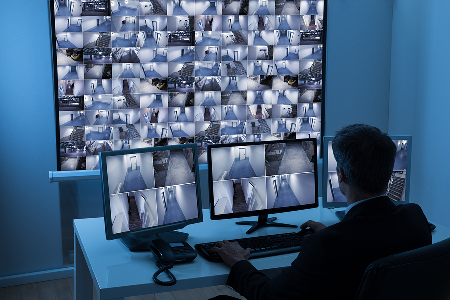 Rear View Of A Man In Control Room Monitoring Multiple Cctv Footage